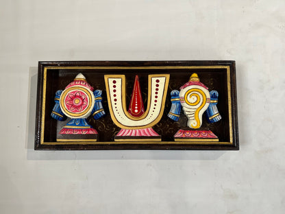 A rectangular hand-painted wooden wall decor piece featuring stylized Devanagari characters 'U' and 'N' in pink, blue, gold, and red, mounted on a light textured wall.